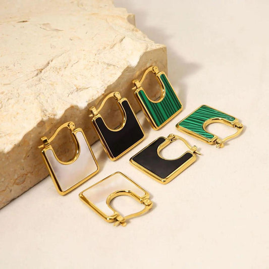A set of square-shaped gold-plated earrings with enamel detailing in black, white, and green, displayed on a neutral background with a textured stone accent.